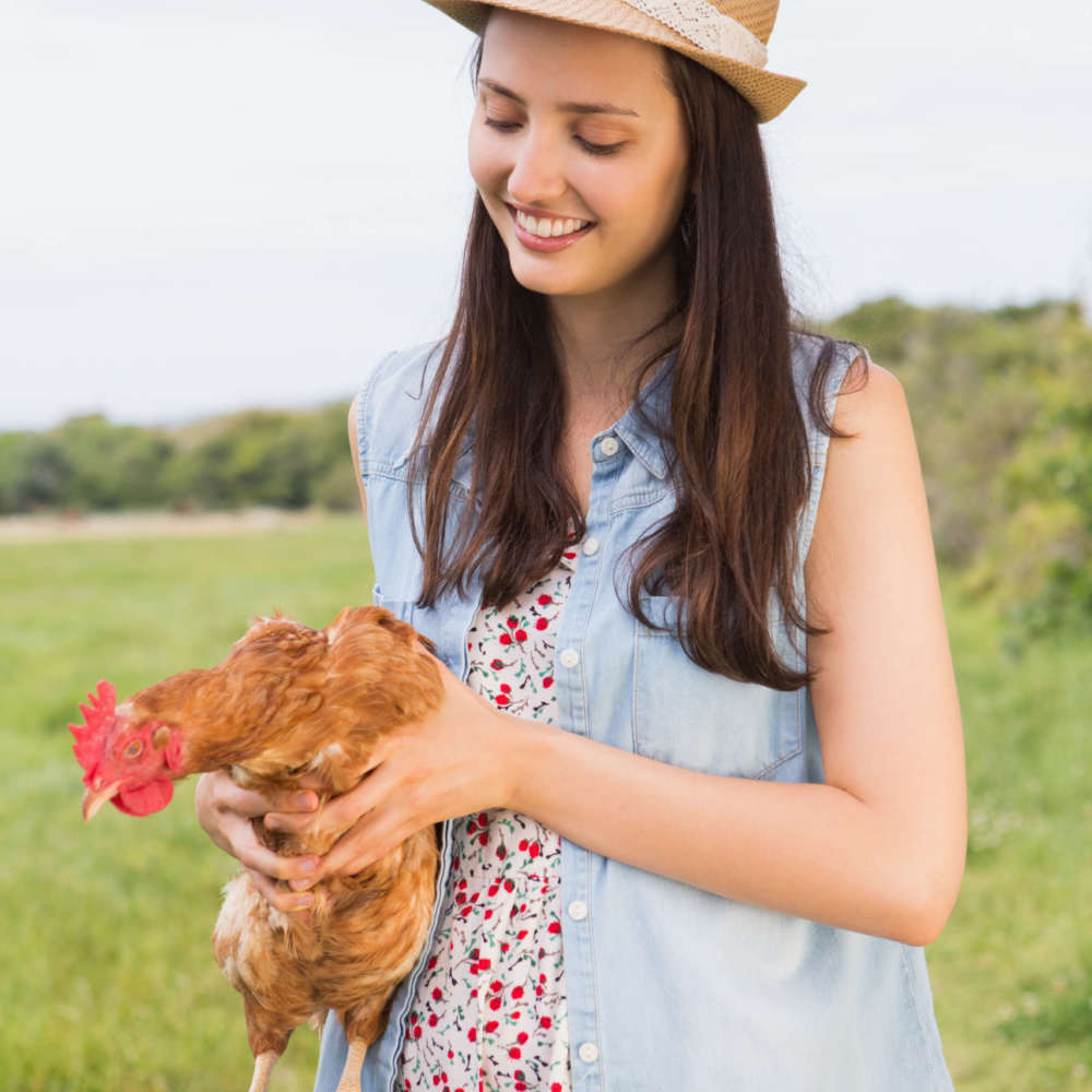 Happy brunette holding her chicken on a sunny day